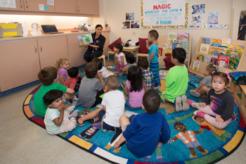 Large group of kids sitting on a mat listening to a story teller